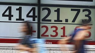 People walk in front of an electronic stock board showing Japan's Nikkei index at a securities firm in Tokyo.