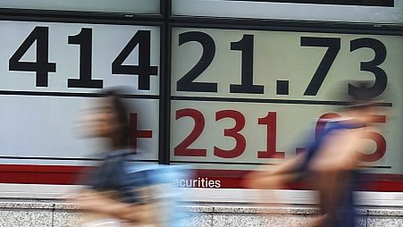 People walk in front of an electronic stock board showing Japan's Nikkei index at a securities firm in Tokyo.