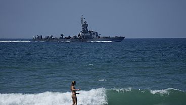 Eine Surferin vor einem israelischen Kriegsschiff vor der Küste von Haifa, 1. August 2024.