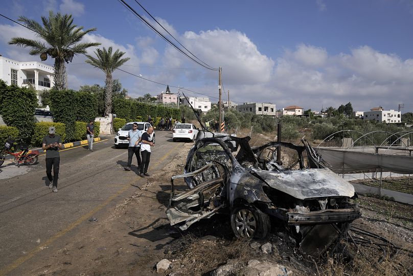 فلسطينيون يتجمعون حول سيارة دمرت في غارة لطائرة بدون طيار قرية زيتا شمال مدينة طولكرم بالضفة الغربية، السبت، 3 أغسطس 2024