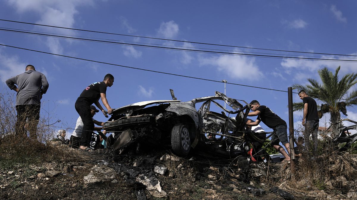 فلسطينيون يتجمعون حول سيارة دمرت في غارة لطائرة بدون طيار في قرية زيتا شمال مدينة طولكرم بالضفة الغربية، السبت، 3 أغسطس 2024. 