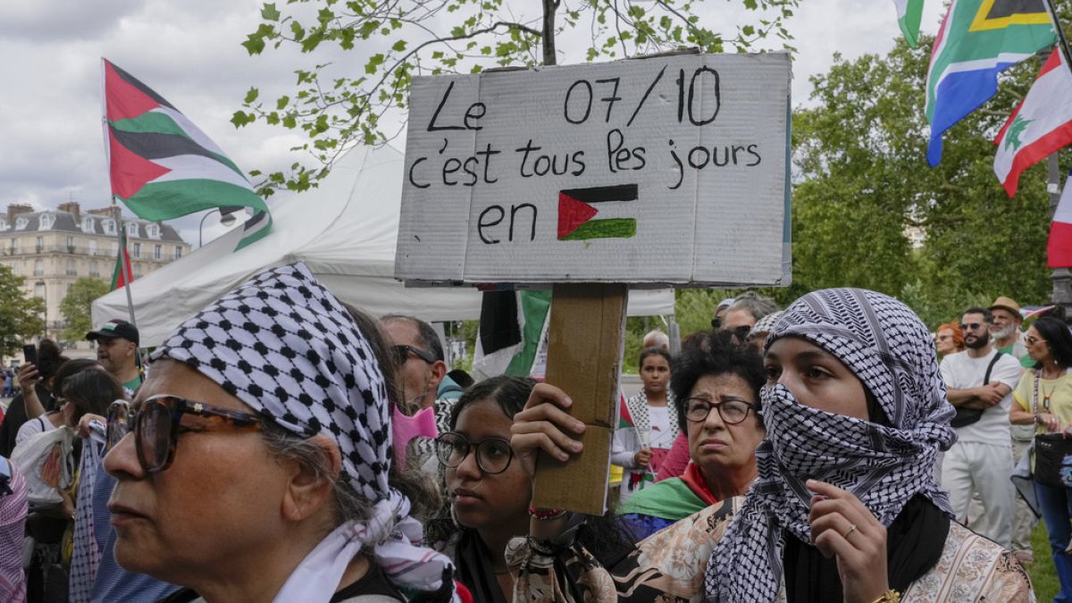 Kefiye giyen bir protestocu, Gazze'deki Filistin halkına destek amacıyla Paris'te düzenlenen gösteride "Filistin'de her gün 7 Ekim" yazılı bir döviz taşıyor, 3 Ağustos 2024