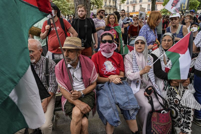 Protesters wearing keffiyehs and holding Palestinian flags sit on a bench during a gathering in support of Palestinian people in Gaza, in Paris, Saturday Aug. 3, 2024.