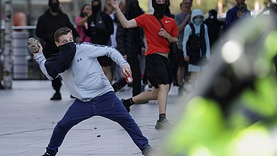 Egy tüntető követ dob a rendőrök felé egy hétvégi angliai tüntetésen