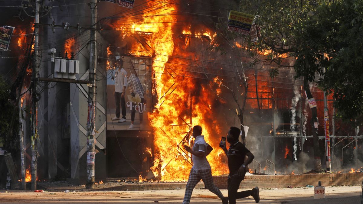 Homens passam por um centro comercial que foi incendiado por manifestantes durante uma manifestação contra a primeira-ministra Sheikh Hasina e o seu governo