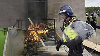 A police officer walks past a fire as trouble flares during an anti-immigration protest outside the Holiday Inn Express in Rotherham, England, Sunday Aug. 4, 2024.