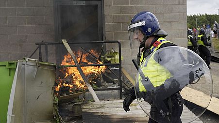 A police officer walks past a fire as trouble flares during an anti-immigration protest outside the Holiday Inn Express in Rotherham, England, Sunday Aug. 4, 2024.