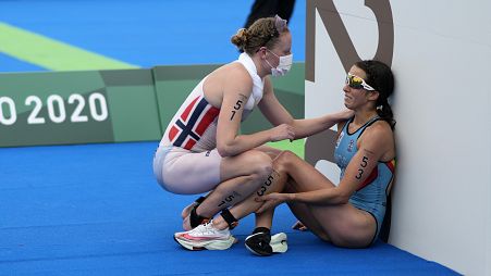 Claire Michel, of Belgium, is assisted by Lotte Miller of Norway after the finish of the women's individual triathlon competition at the 2020 Summer Olympics.