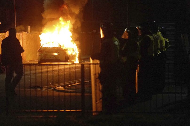 A police car burns as officers are deployed on the streets of Hartlepool, England, following a violent protest in the wake of the killing of three girls