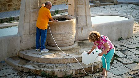 Antonino Contino, left, and his wife Antonella Croce fill jerry cans with water for daily use at Agrigento's only public fountain in Sicily, on 17 July 2024.