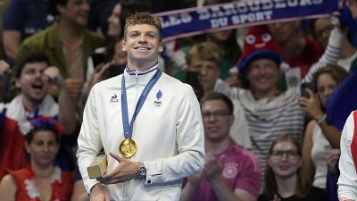 Leon Marchand of France, reacts as he stands on the podium after receiving his gold medal for the men's 200-meter individual medley final at the 2024 Summer Olympics.