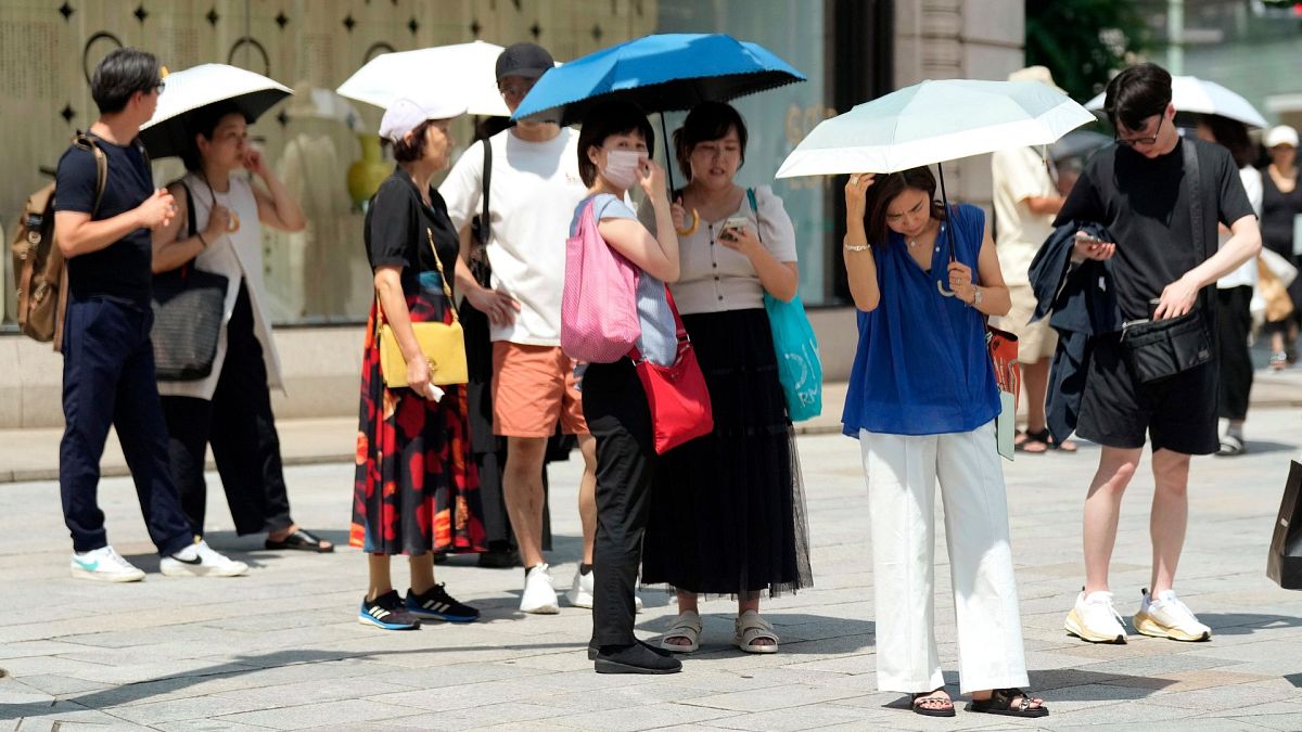 Pedestrian holding parasols stand under an intense sun at Ginza shopping street in Tokyo, on 8 July 2024.