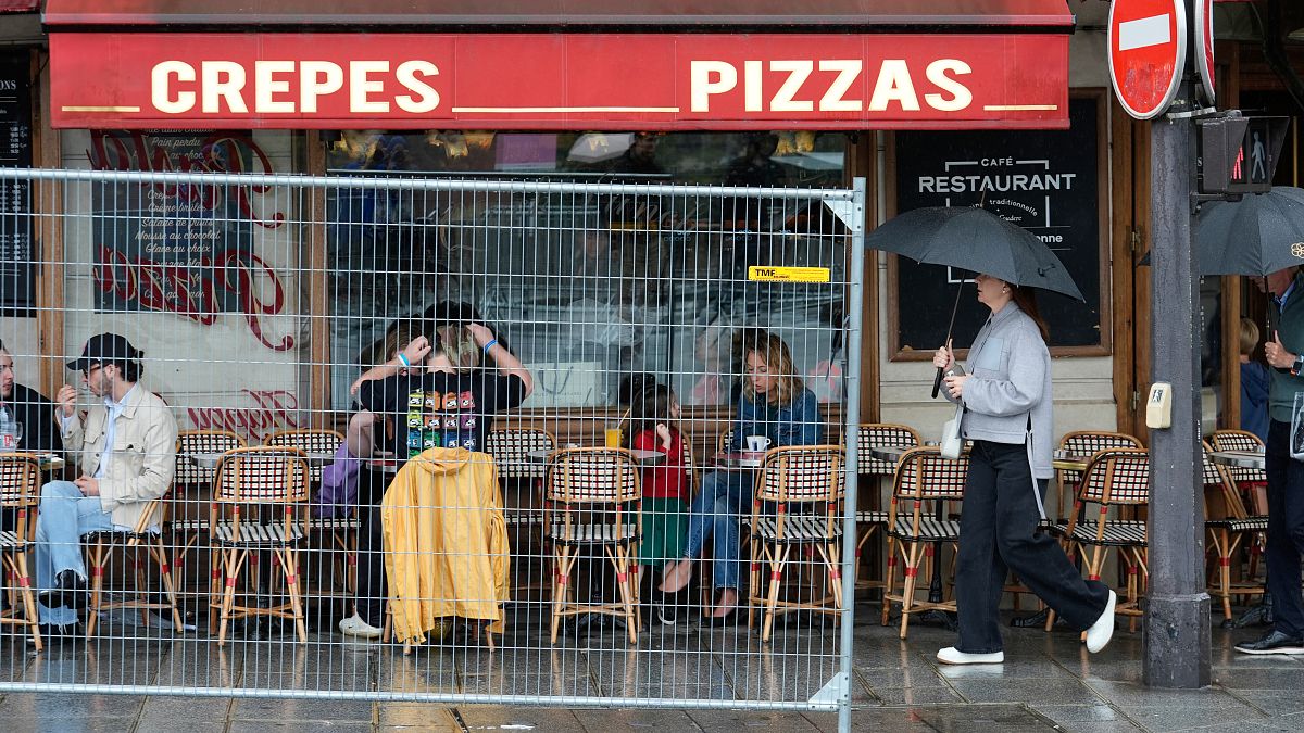 Patrons sit outside a restaurant behind a remaining security barrier on a street along the Seine River, now opened to foot traffic after the Olympic Games' opening ceremony.