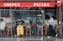 Patrons sit outside a restaurant behind a remaining security barrier on a street along the Seine River, now opened to foot traffic after the Olympic Games' opening ceremony.