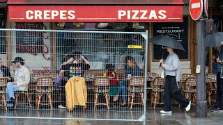 Besucher sitzen vor einem Restaurant hinter einer verbleibenden Sicherheitsbarriere in einer Straße an der Seine, die nach der Eröffnungsfeier der Olympischen Spiele für den Fußgängerverkehr freigegeben wurde.