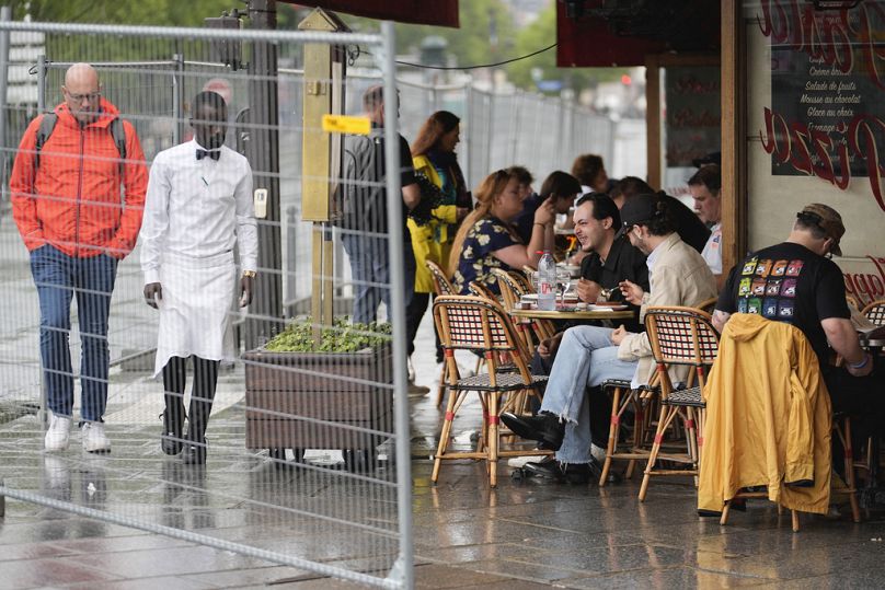 Os clientes sentam-se à porta de um restaurante por detrás de algumas barreiras de segurança remanescentes numa rua ao longo do rio Sena.