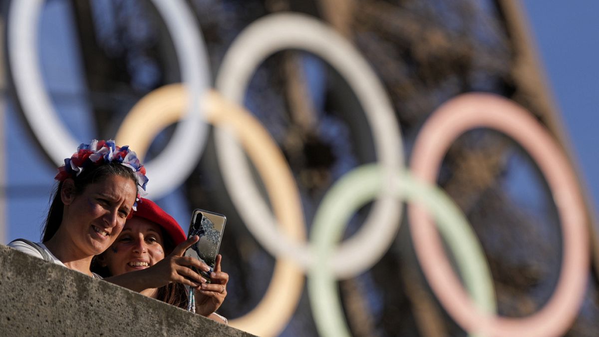 Une personne prend un selfie avec les anneaux olympiques sur la Tour Eiffel pendant les Jeux Olympiques d'été de 2024, le mardi 6 août 2024, à Paris, en France.