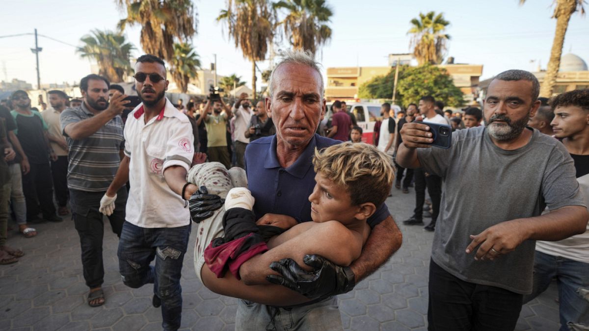 Um homem palestiniano carrega uma criança ferida após um ataque aéreo israelita em Deir al Balah, na Faixa de Gaza, terça-feira, 6 de agosto de 2024.