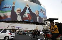 Vehicles drive past a huge banner showing the late Hamas leader Ismail Haniyeh, left, who was killed in an assassination last week, joining hands with Iranian President Masoud