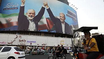 Vehicles drive past a huge banner showing the late Hamas leader Ismail Haniyeh, left, who was killed in an assassination last week, joining hands with Iranian President Masoud