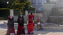 A couple relax by a fountain in front of a matador and traditional dress cutouts for tourists to pose behind for photos in Madrid, Spain, Friday, July 19, 2024.