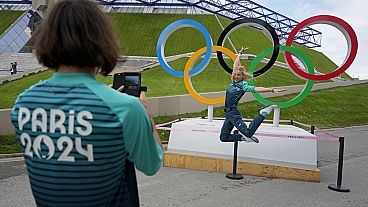 Olympic volunteer Manuella Mallam has her photo taken with the Olympic rings outside Bercy Arena ahead of the 2024 Summer Olympics, Tuesday, July 23, 2024, in Paris, France.