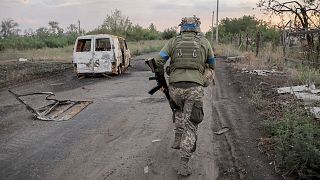 a serviceman of the 24th Mechanised Brigade runs past a damaged car at the frontline town of Chasiv Yar, Donetsk region, 6 August 2024