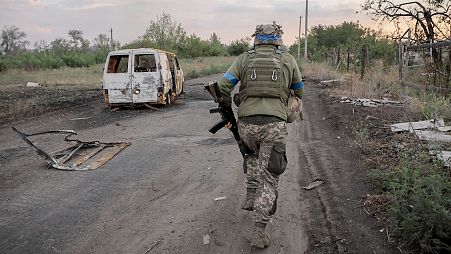 un soldat de la 24e brigade mécanisée passe devant une voiture endommagée dans la ville de Chasiv Yar, dans la région de Donetsk, le 6 août 2024.