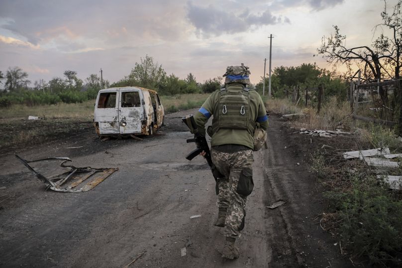 In this photo provided by Ukraine's 24th Mechanised Brigade press service, a serviceman of the 24th Mechanised Brigade runs past a damaged car at the frontline town of Chasiv.