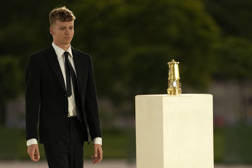 French swimmer Leon Marchand walks toward a plinth where a lantern containing the Olympic flame sits in the Tuileries garden on the final day of the 2024 Summer Olympics 