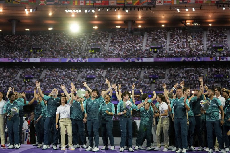 Voluntários acenam durante a cerimónia de encerramento dos Jogos Olímpicos de verão de 2024 no Stade de France, domingo, 11 de agosto de 2024, em Saint-Denis, França