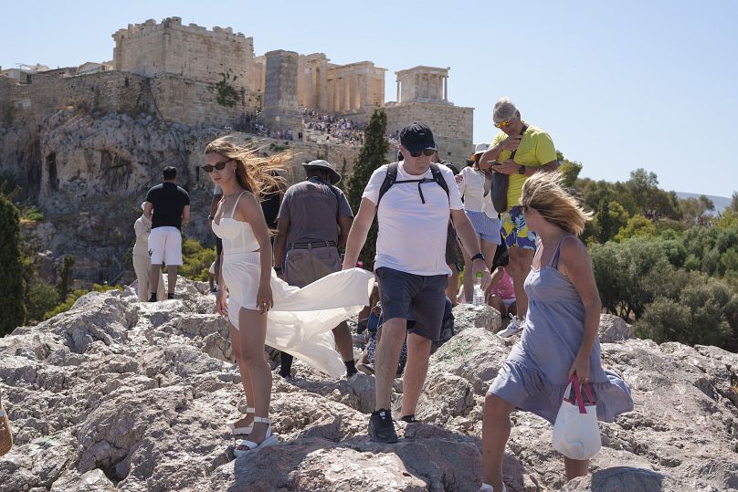 Des touristes sur la colline d'Areopagous devant l'ancienne colline de l'Acropole lors d'une journée chaude à Athènes, le mercredi 17 juillet 2024.