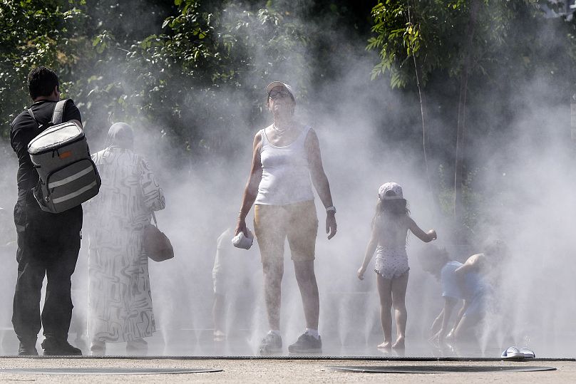 Pessoas refrescam-se num chuveiro público de água nebulizada no centro de Paris, França.