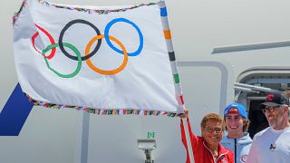 Los Angeles Belediye Başkanı Karen Bass, solda, 12 Ağustos 2024 Pazartesi günü Los Angeles Uluslararası Havalimanı'nda resmi Olimpiyat bayrağını tutuyor.