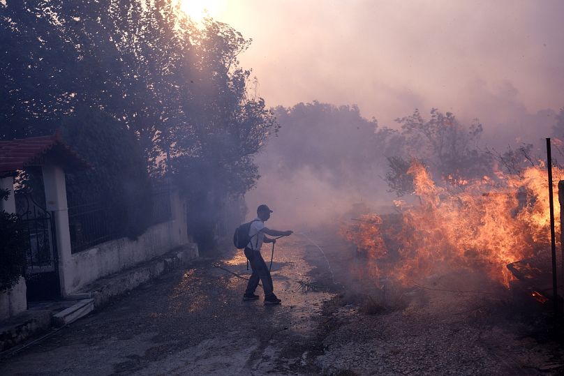 Un homme tente d'éteindre les flammes près d'une maison lors d'un incendie dans le nord d'Athènes, en Grèce, le lundi 12 août 2024.