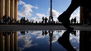 The Eiffel Tower is reflected in a puddle as people walk past at the Trocadero square, in Paris, France, Tuesday, Oct. 24, 2023. (AP Photo/Pavel Golovkin)