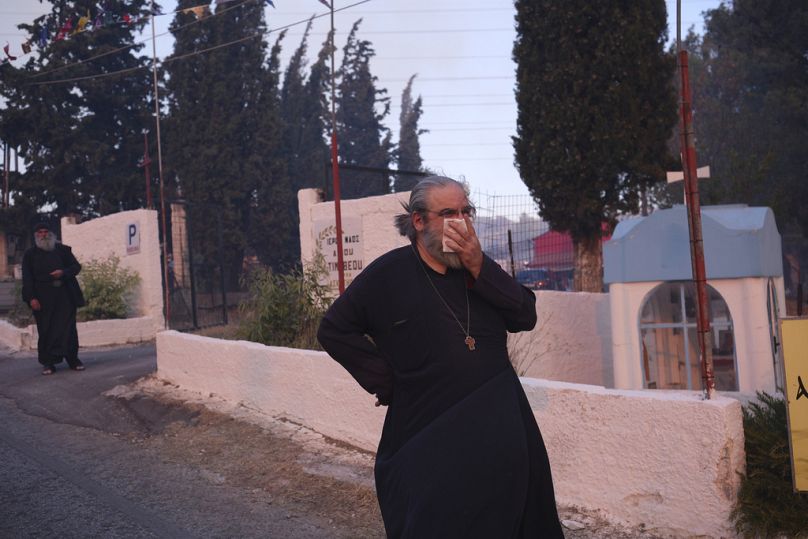 Two monks stand outside a monastery during a fire in northern Athens, Monday, Aug. 12, 2024, as hundreds of firefighters tackle a major wildfire raging out of control.