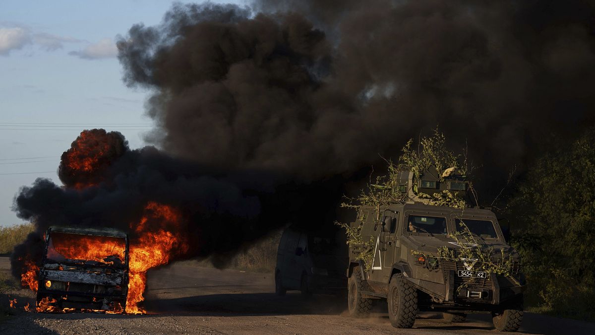 A Ukrainian armoured military vehicle travels past a burned car near the Russian-Ukrainian border in the Sumy region.