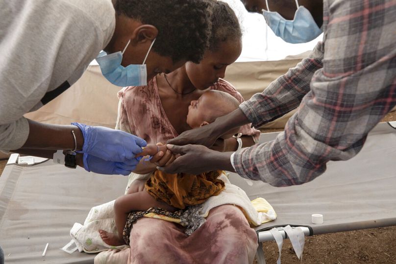 A woman who fled the conflict in Ethiopia's Tigray region, holds her malnourished and severely dehydrated baby as nurses give him IV fluids, at an MSF clinic in Sudan in 2020