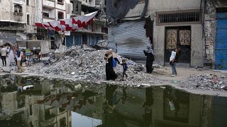 Displaced Palestinians walk next a dark streak of sewage flowing into the streets of the southern town of Khan Younis, July 4, 2024