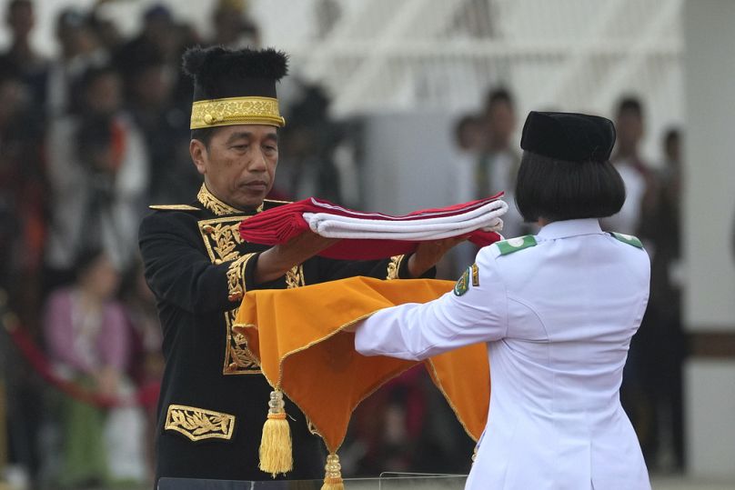 O Presidente indonésio Joko Widodo, à esquerda, entrega a bandeira nacional vermelha e branca a um portador para ser hasteada durante a cerimónia que assinala o 79.º