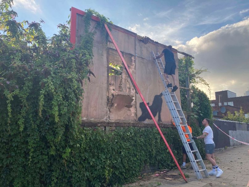 A hirdetőtáblát szerelik szét, amelyre Banksy egy nagymacskát festett, 2024. augusztus 10-én