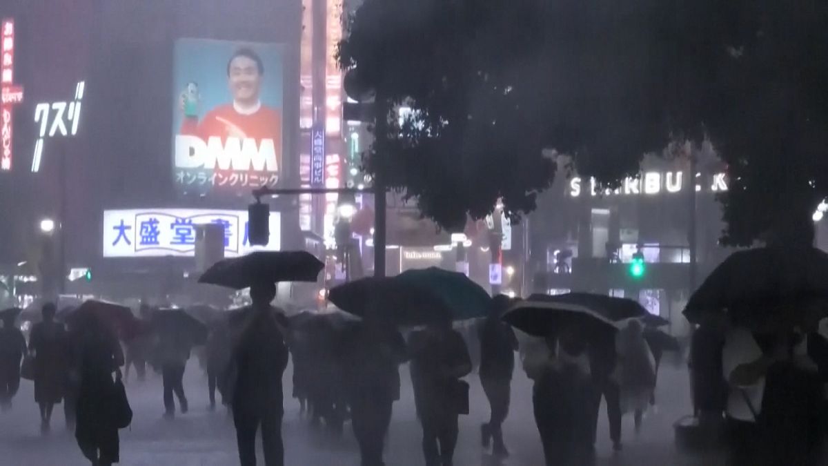 People rushing with umbrellas through heavy rain near Shibuya station