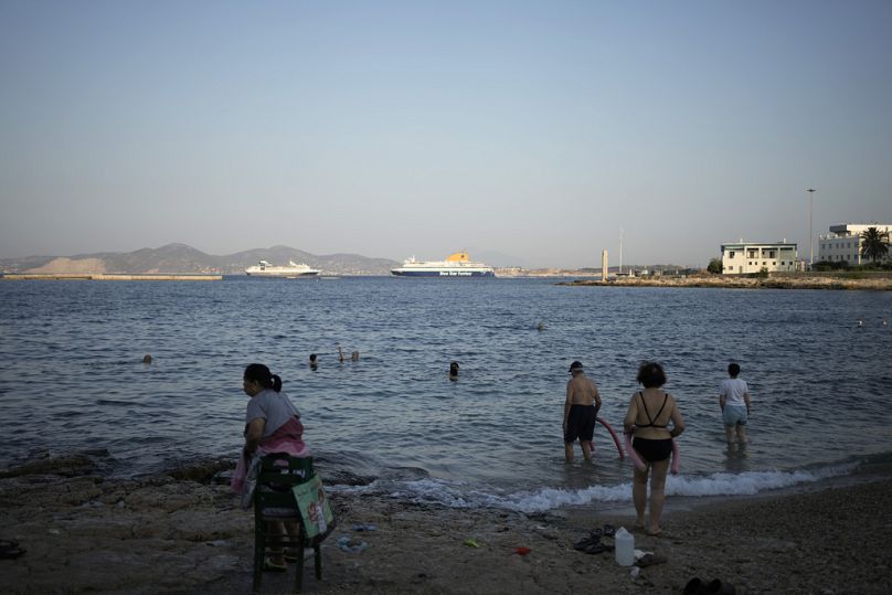 People swim on a small beach, during a warm morning at Athens' port city of Piraeus.