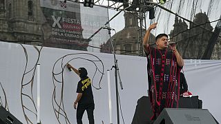 O artista mexicano-triqui Carlos CGH, vestindo um “gabán” preto e vermelho, uma peça de vestuário nativa do povo Triqui,  na Cidade do México, terça-feira, 6 de agosto de 2024