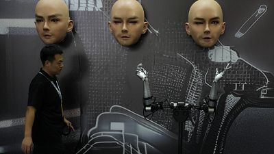 A worker walks past various kinds of human-like robots at the World Robot Conference held in Beijing.