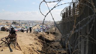 فلسطينيون نازحون جراء الهجوم الجوي والبري الإسرائيلي على قطاع غزة يجلسون بجوار السياج الحدودي مع مصر في رفح، الأربعاء، 24 يناير 2024