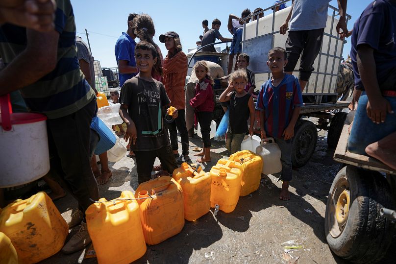 نازحون فلسطينيون يصطفون لجمع المياه في دير البلح وسط قطاع غزة، الجمعة، 23 أغسطس/آب 2024