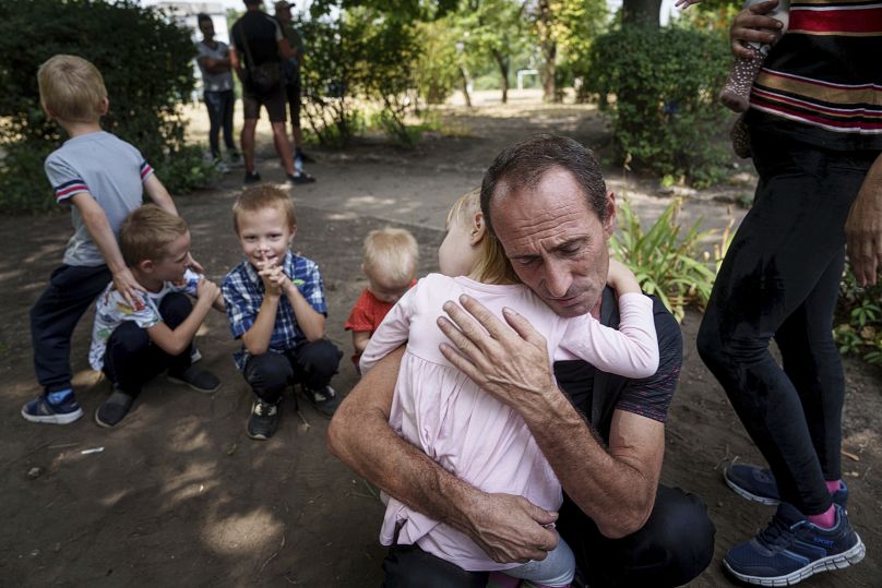 A father hugs his daughter, his other children nearby, as they wait for evacuation in Pokrovsk, Donetsk region, Ukraine, Friday, Aug. 23, 2024.