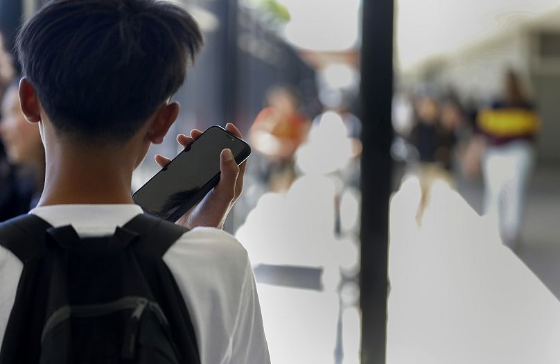 A student uses their cell phone after unlocking the pouch that secures it from use during the school day in the US.